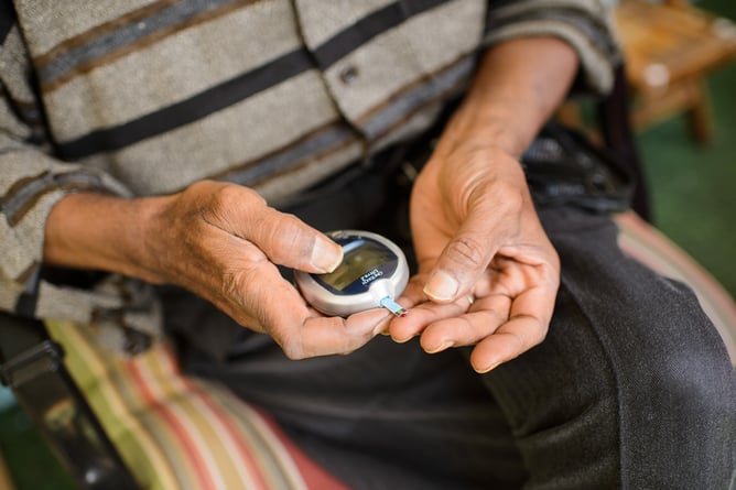 Patient's hands holding a glucose monitor and performing fingerstick to check blood sugar