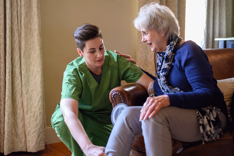 Caregiver dressed in green scrubs assessing the mobility of an elderly female patient’s right leg