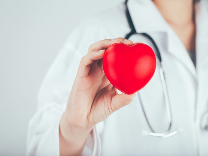Close up of a doctor with a stethescope holding a red heart shape up