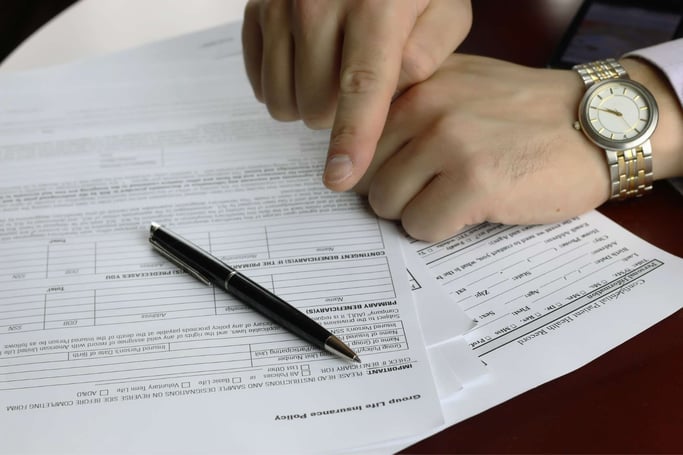 Insurance coverage paperwork, a pen, and a hand pointing at terms