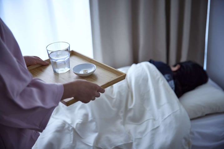person lying in bed and tray of food being offered