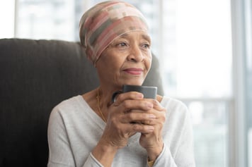 Older woman with head wrap looking thoughtful and drinking coffee