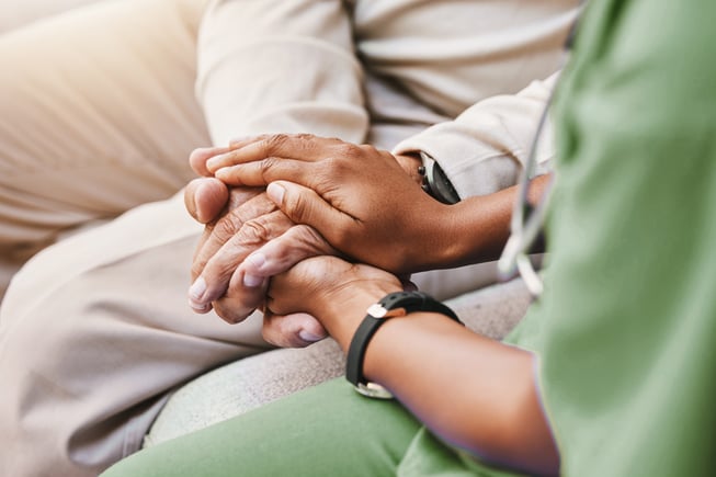 nurse in green scrubs holding patient hand between hers