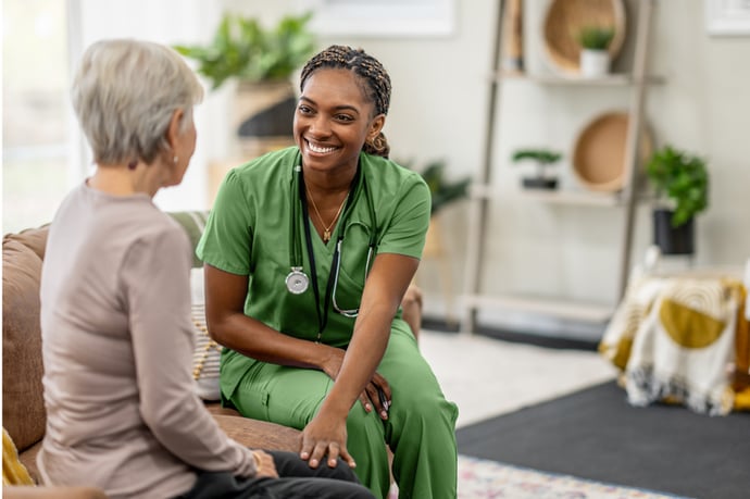 smiling nurse in green scrubs talking to older patient