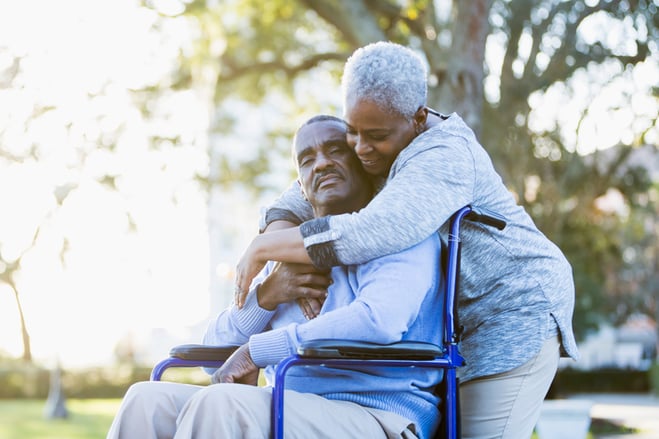 Elderly woman hugging an elderly man in a wheelchair