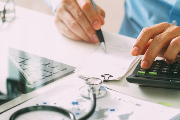 image of a calculator, stethescope, and hand holding a pen